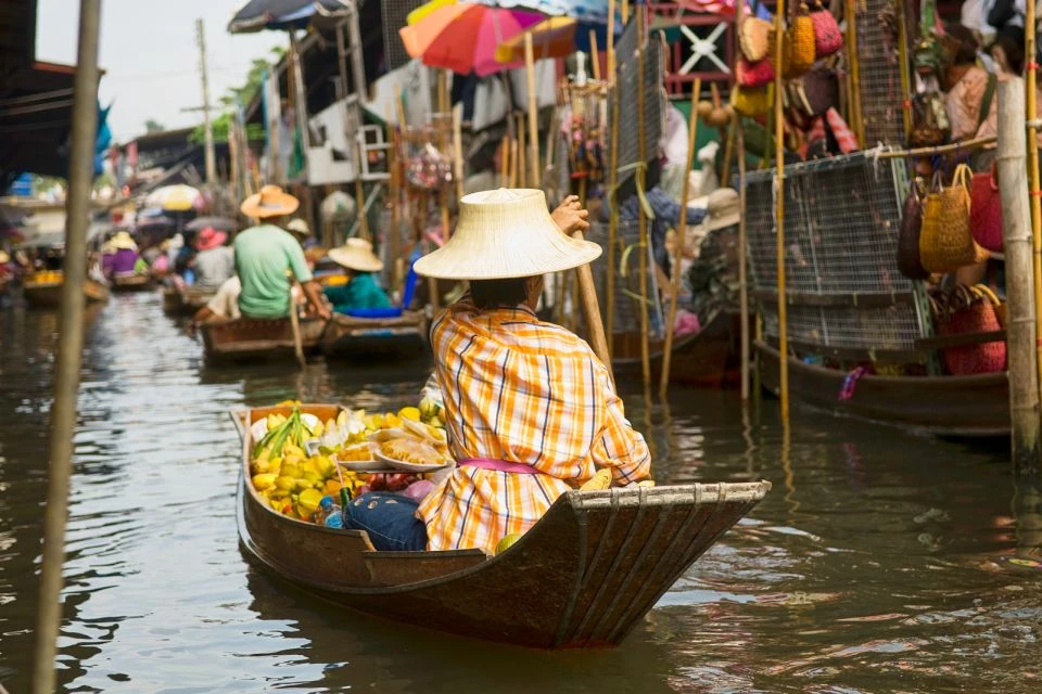 A person navigates through a bustling floating market - Thai Pass