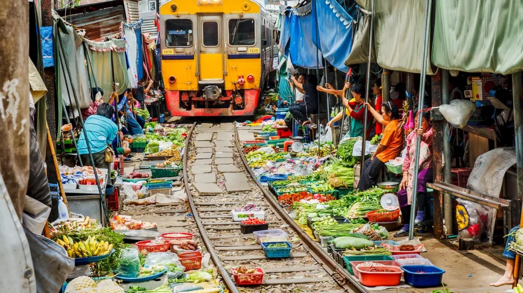 A yellow train approaches the Maeklong railway market in Bangkok - Thai Pass