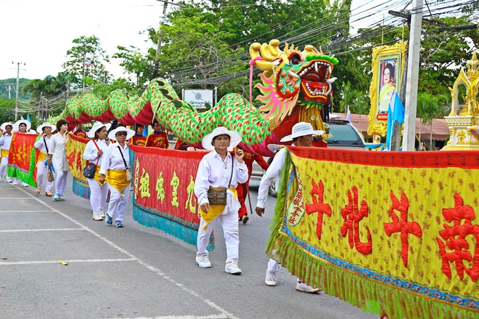 A group of people in white outfits and hats parade with a green and red dragon float - Thai Pass